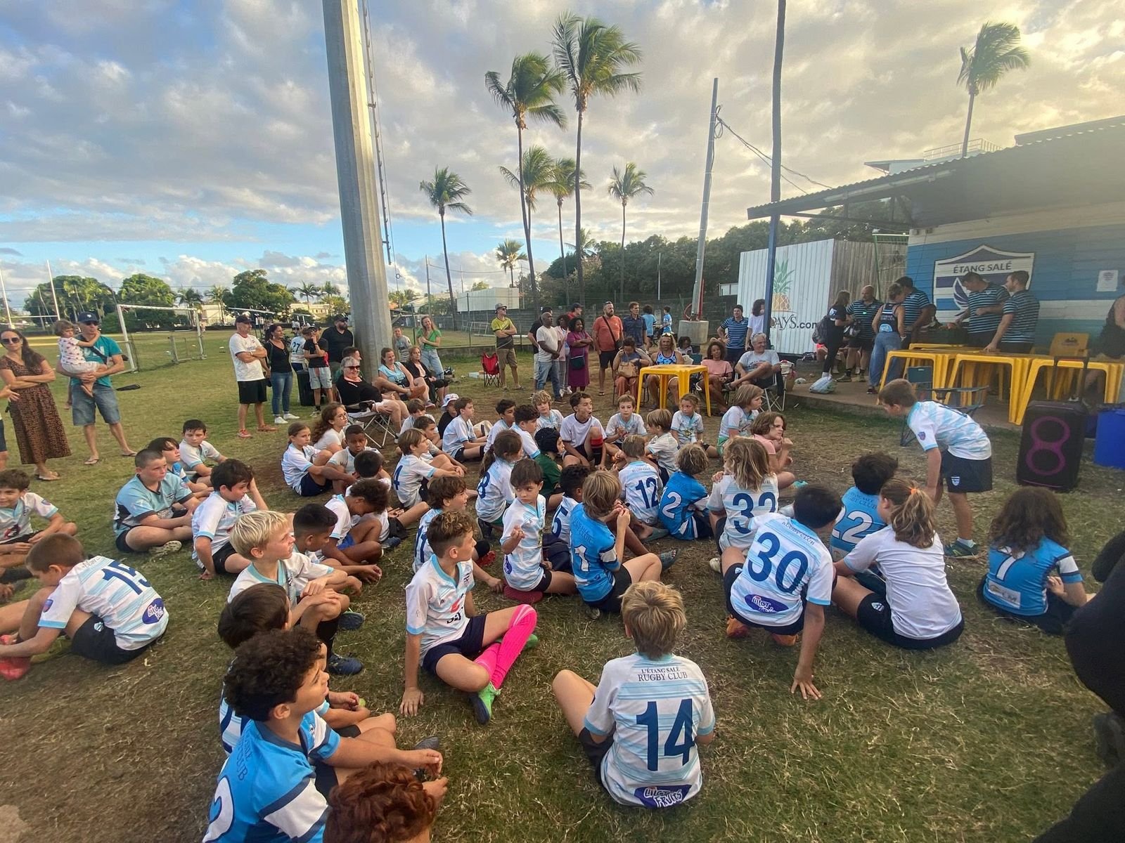 Les enfants de l'école de rugby rassemblés dans l'herbe devant le club-house, entourés de leurs parents